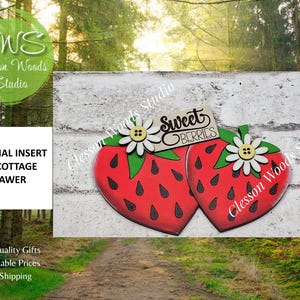 May include: A seasonal insert for a cottage drawer featuring two red strawberries with black seeds, green leaves, and white daisy flowers with yellow button centers. A wooden sign attached to the top reads Sweet Berries in black script lettering.