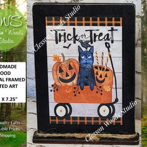 May include: Handmade wood framed art with a Halloween theme. The image features a black cat in an orange wagon with a pumpkin and a jack-o'-lantern bucket. The text "Trick or Treat" is at the top. The frame measures 5.50" x 7.25".