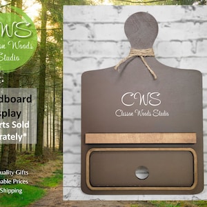 May include: A brown wooden breadboard display with a shelf and a drawer. The display has a cutout for a bread knife and is labeled "CWS Clesson Woods Studio".