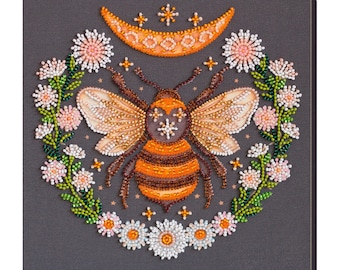 May include: A beaded artwork featuring a bee with orange and brown stripes, surrounded by a wreath of white and pink flowers and a crescent moon.