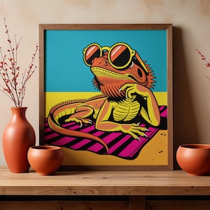 May include: A framed square art print featuring a stylized orange bearded dragon wearing yellow-rimmed sunglasses, reclining on a pink and black striped towel against a blue and yellow background, displayed with two terracotta vases.