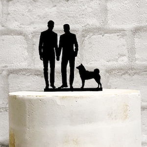 May include: Black silhouette cake topper of two grooms holding hands with a dog standing between them.