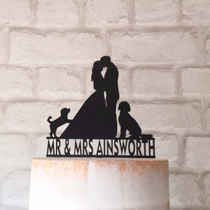May include: Black silhouette cake topper featuring a bride and groom kissing, with two dogs on either side. The topper includes the text "MR & MRS AINSWORTH".