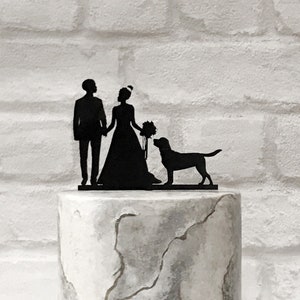 May include: Black silhouette cake topper of a bride and groom holding hands with a black dog standing between them.
