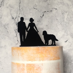 Peut inclure: Topper de gâteau en silhouette noire d'une mariée et d'un marié se tenant la main avec un chien debout derrière eux.