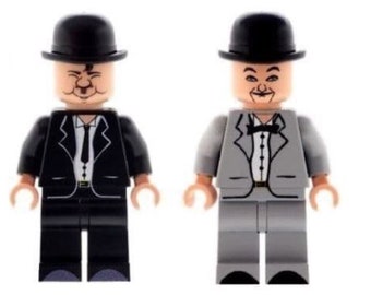 May include: Two LEGO minifigures of men wearing black bowler hats and suits. One minifigure is wearing a black suit and the other is wearing a gray suit.