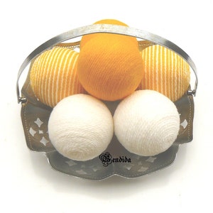 May include: A silver metal basket with a handle holds six yarn balls. Four of the balls are white and two are yellow with white stripes.