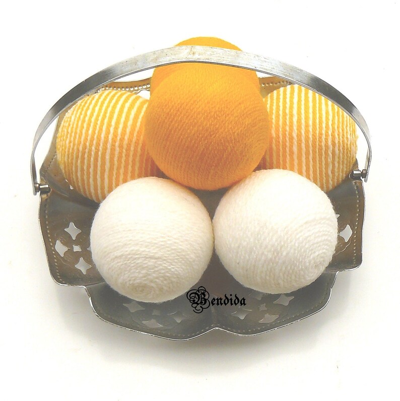 May include: A silver metal basket with a handle holds six yarn balls. Four of the balls are white and two are yellow with white stripes.