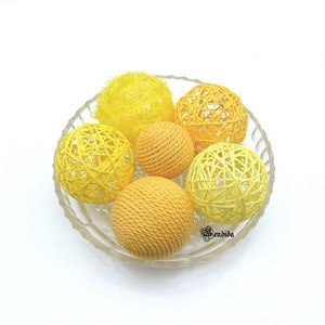 May include: A glass bowl filled with yellow and orange woven balls. The balls are made of natural fibres and have a soft, textured surface.