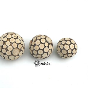 May include: Three wooden spheres made of small, round, wooden pieces. The spheres are different sizes and are arranged in a row from largest to smallest.