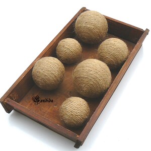 May include: Six brown twine balls in a wooden tray. The balls are made of natural twine and are arranged in a row. The tray is made of wood and has a natural finish.