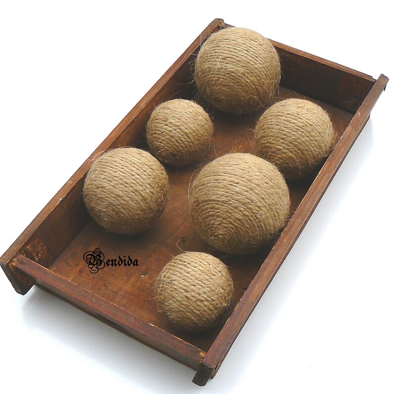 May include: Six brown twine balls in a wooden tray. The balls are made of natural twine and are arranged in a row. The tray is made of wood and has a natural finish.