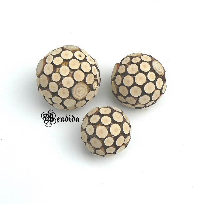 May include: Three round wooden ornaments made of small wood circles. The ornaments are beige and brown and have a natural wood finish.