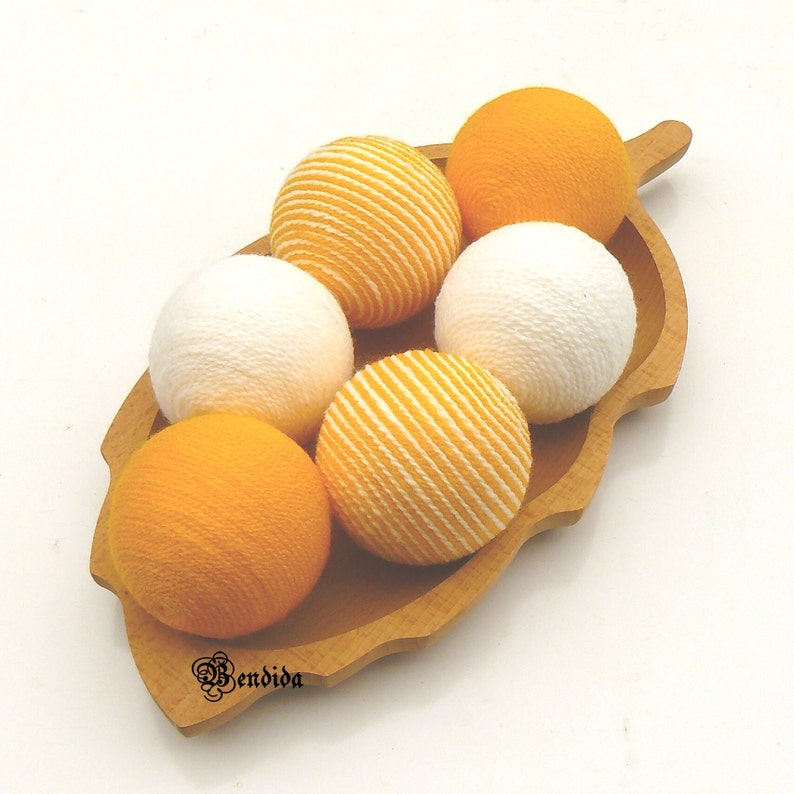 May include: Six yarn balls in a wooden bowl. Three balls are white and three are yellow with white stripes.