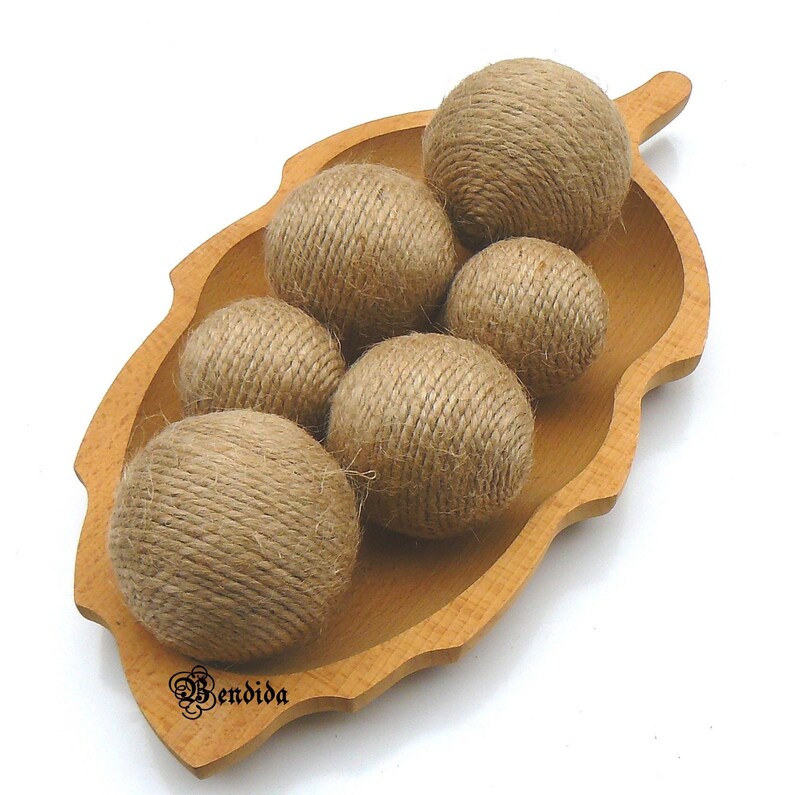 May include: A wooden leaf-shaped bowl filled with six brown twine balls. The bowl is made of light brown wood and has a smooth, polished finish.