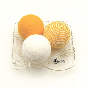 May include: Three yarn balls in a glass dish. One ball is white, one is yellow, and one is yellow with white stripes.