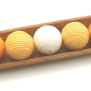 May include: Four yarn balls in a wooden tray. Two balls are yellow, one is white, and one is yellow with white stripes.