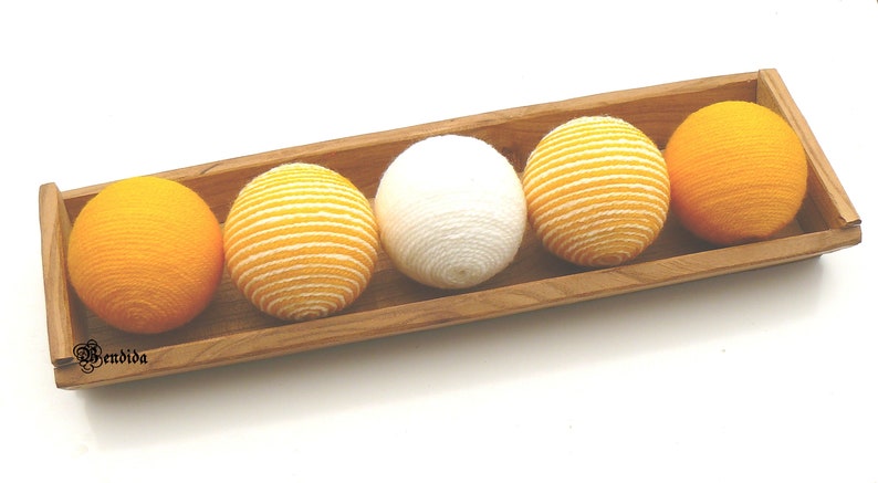 May include: Four yarn balls in a wooden tray. Two balls are yellow, one is white, and one is yellow with white stripes.