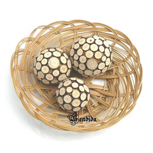 May include: Three decorative spheres made of wood with a circular pattern, displayed in a woven wicker basket.