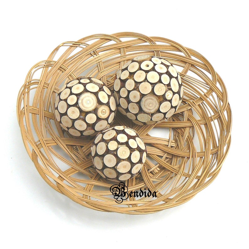 May include: Three decorative spheres made of wood with a circular pattern, displayed in a woven wicker basket.