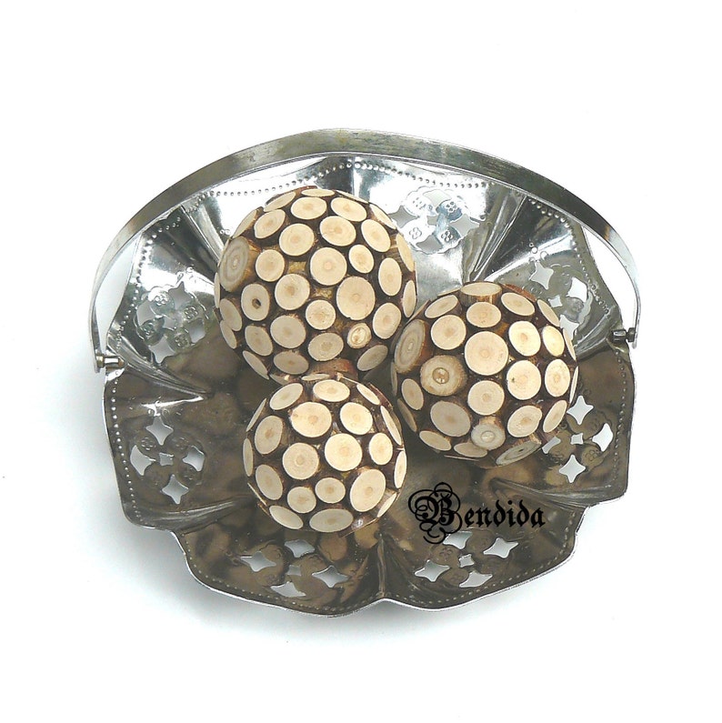 May include: Three decorative wooden balls with a circular pattern in a silver metal bowl. The balls are white with brown circles.