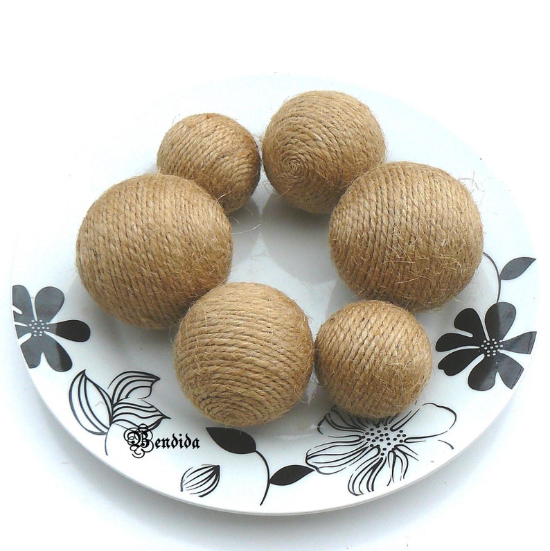 May include: Six brown, round, twine-wrapped balls on a white plate with a black floral design.