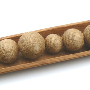 May include: A wooden tray with six round balls made of natural twine. The balls are arranged in a row, with the largest ball at the back and the smallest ball at the front. The tray is made of light brown wood and has a natural finish.