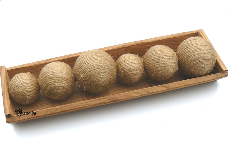 May include: A wooden tray with six round balls made of natural twine. The balls are arranged in a row, with the largest ball at the back and the smallest ball at the front. The tray is made of light brown wood and has a natural finish.