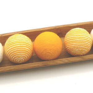 May include: Four yarn balls in a wooden tray. Two balls are white and two are yellow with white stripes.