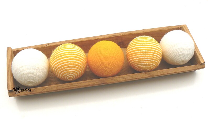 May include: Four yarn balls in a wooden tray. Two balls are white and two are yellow with white stripes.
