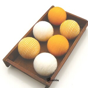 May include: Six decorative balls in a wooden tray. Three balls are white and three are yellow with white stripes.