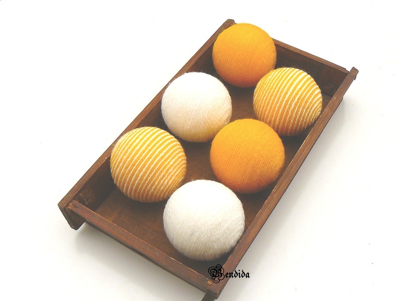 May include: Six decorative balls in a wooden tray. Three balls are white and three are yellow with white stripes.