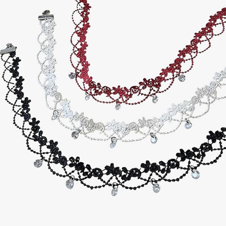 May include: Three lace chokers in black, white, and deep red. Each choker features an intricate floral pattern with a lattice-style weave and delicate dangling clear crystal-like charms attached along the bottom edge, secured with metal clasps.