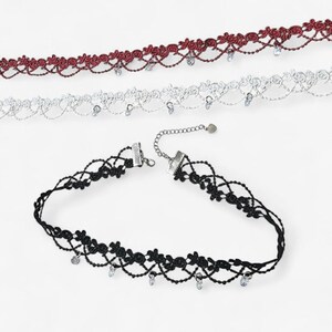 May include: Three lace chokers in burgundy, white, and black. Each choker features a floral pattern with a scalloped edge and small, dangling clear crystal-like beads. The black choker includes a silver-toned metal chain extender with a small charm.