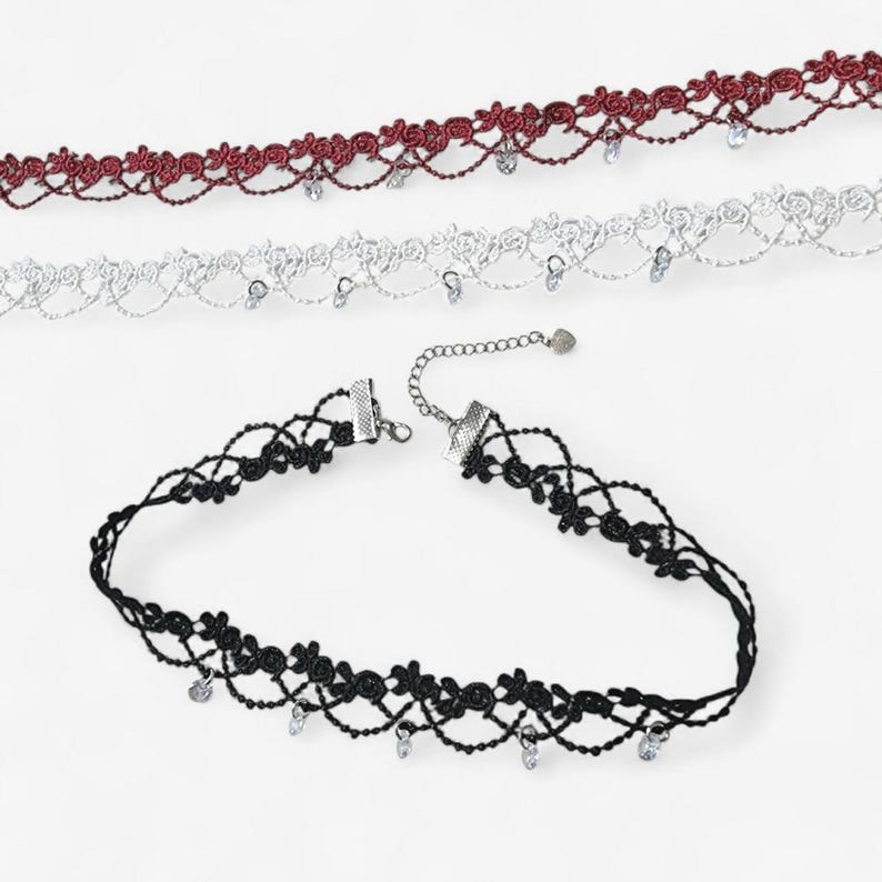 May include: Three lace chokers in burgundy, white, and black. Each choker features a floral pattern with a scalloped edge and small, dangling clear crystal-like beads. The black choker includes a silver-toned metal chain extender with a small charm.