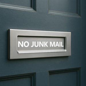 May include: A silver metal letterbox with the words "NO JUNK MAIL" in white lettering is mounted on a dark blue door. The door has a paneled design. The letterbox is rectangular and has a simple, modern design.