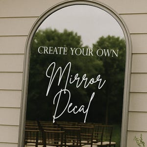 May include: An arched mirror with a silver frame. The mirror reflects a wedding ceremony setup with chairs and greenery. White script on the mirror reads "CREATE YOUR OWN Mirror Decal."