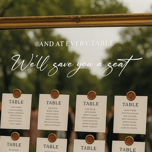 May include: A gold framed seating chart with the text "And at every table, We'll save you a seat." Twelve cards are displayed, each labeled "TABLE" and listing names. The cards are affixed with brown wax seals.