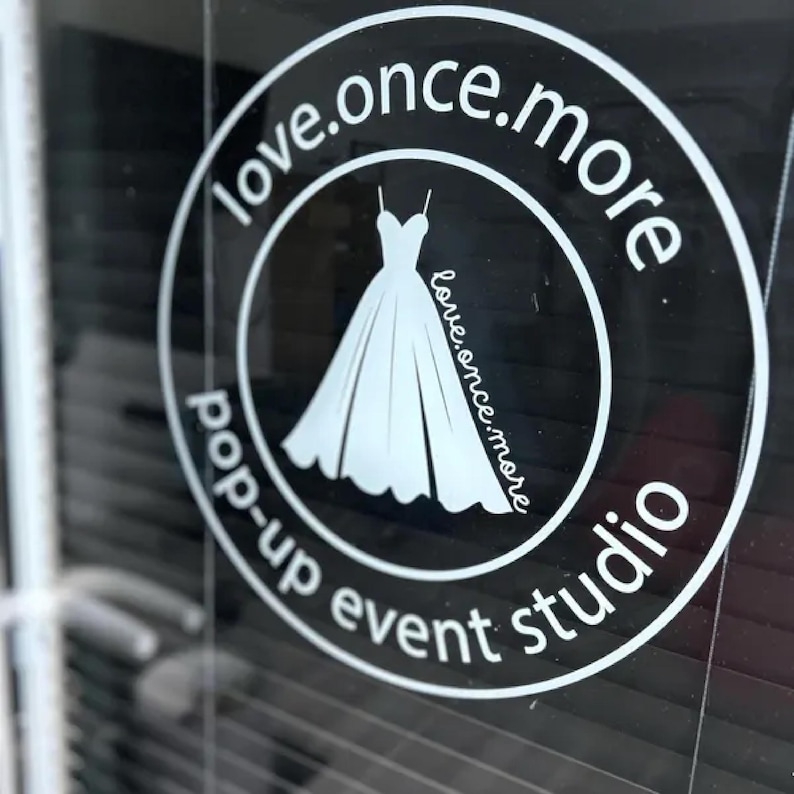 Może przedstawiać: Białe okrągłe logo na ciemnym tle. Logo zawiera słowa "love.once.more" w okrągłym wzorze, otaczające białą ilustrację sukni ślubnej. Zawiera r&oacute;wnież słowa "pop-up event studio".
