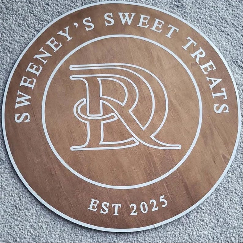 Może przedstawiać: Okrągły drewniany znak z napisem "Sweeney's Sweet Treats" w białym kolorze. Znak posiada stylizowany biały monogram "SR" na środku oraz napis "EST 2025" na dole. Znak ma fakturę słoj&oacute;w drewna i brązowy kolor.