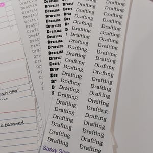 May include: A sheet of rectangular adhesive labels featuring the word Drafting printed in black ink. The sheet includes the text Sassy Sisters Stickers and the code S-01a in purple at the bottom. A purple pen rests at the top of the sticker sheet.