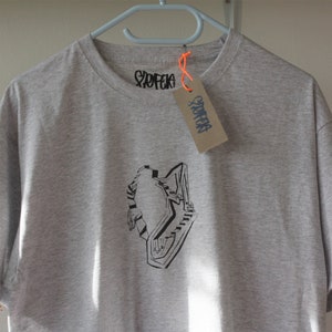 May include: A gray t-shirt with a black and white graphic of a person in a maze. The shirt has a tag that says "Storefak" on it.