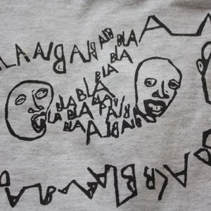 May include: A gray t-shirt with a black graphic print of two faces with open mouths and the words "bla bla bla" and "la la la" repeated around the faces.
