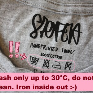 May include: A gray t-shirt with a black care label that says "SOFEA HANDPRINTED THINGS 100% COTTON". The care label includes symbols for machine washing at 30 degrees Celsius, no bleaching, ironing, and no tumble drying. The text below the image says "Wash only up to 30&deg;C, do not dry clean. Iron inside out :-) "