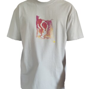 May include: A light gray t-shirt with a crew neck and short sleeves. The shirt features a colorful abstract design in shades of red, orange, and yellow on the front. The design appears to be a stylized figure or shape.