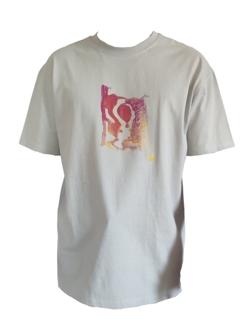 May include: A light gray t-shirt with a crew neck and short sleeves. The shirt features a colorful abstract design in shades of red, orange, and yellow on the front. The design appears to be a stylized figure or shape.