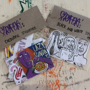 May include: Two clear plastic bags containing stickers, each topped with a brown cardboard header. One header reads "STIFLER'S COLOURFUL STICKERPACK" and the other "STIFLER'S BLACK AND WHITE STICKER-PACK". The stickers feature various illustrations.