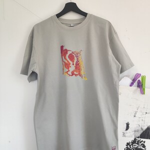 May include: A light gray t-shirt with a colorful abstract design on the front. The design features red, yellow, and orange hues. The word "SPARKS" is printed in pink on the lower right side of the shirt.