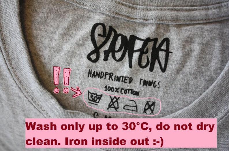 May include: Close-up of a gray t-shirt label with the word "SOPEA" in black script. The label reads "HANDPRINTED THINGS" and "100% COTTON." Washing instructions include a symbol for washing at 30&deg;C, do not dry clean, and iron inside out.