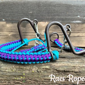 May include: A turquoise and purple braided rope halter with a silver and brown metal bit. The bit is a curb bit with a chain attached to the bottom. The halter is made of braided rope and is designed for horses.